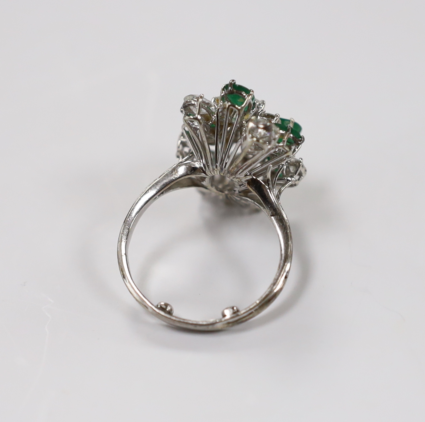 A modern white metal emerald and diamond cluster set dress ring, size R/S, the shank with two sizing spheres, gross weight 8 grams.